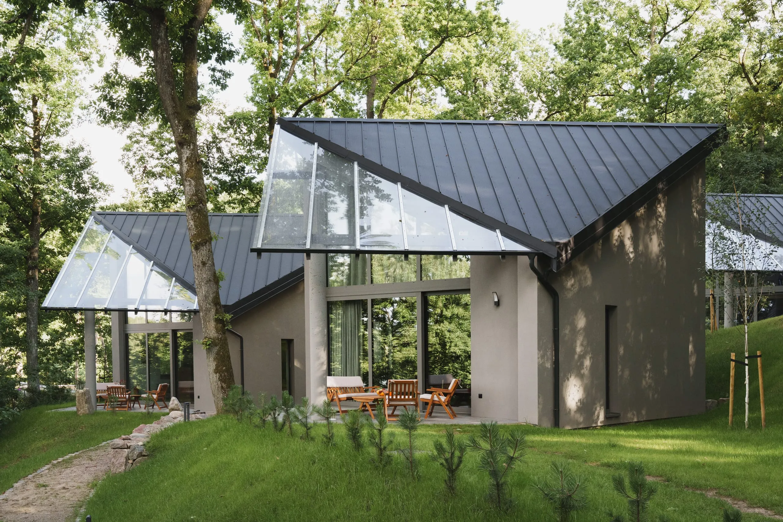 A cabin's steep dark roof and glazed gable standing over a terrace of wooden chairs among the trees