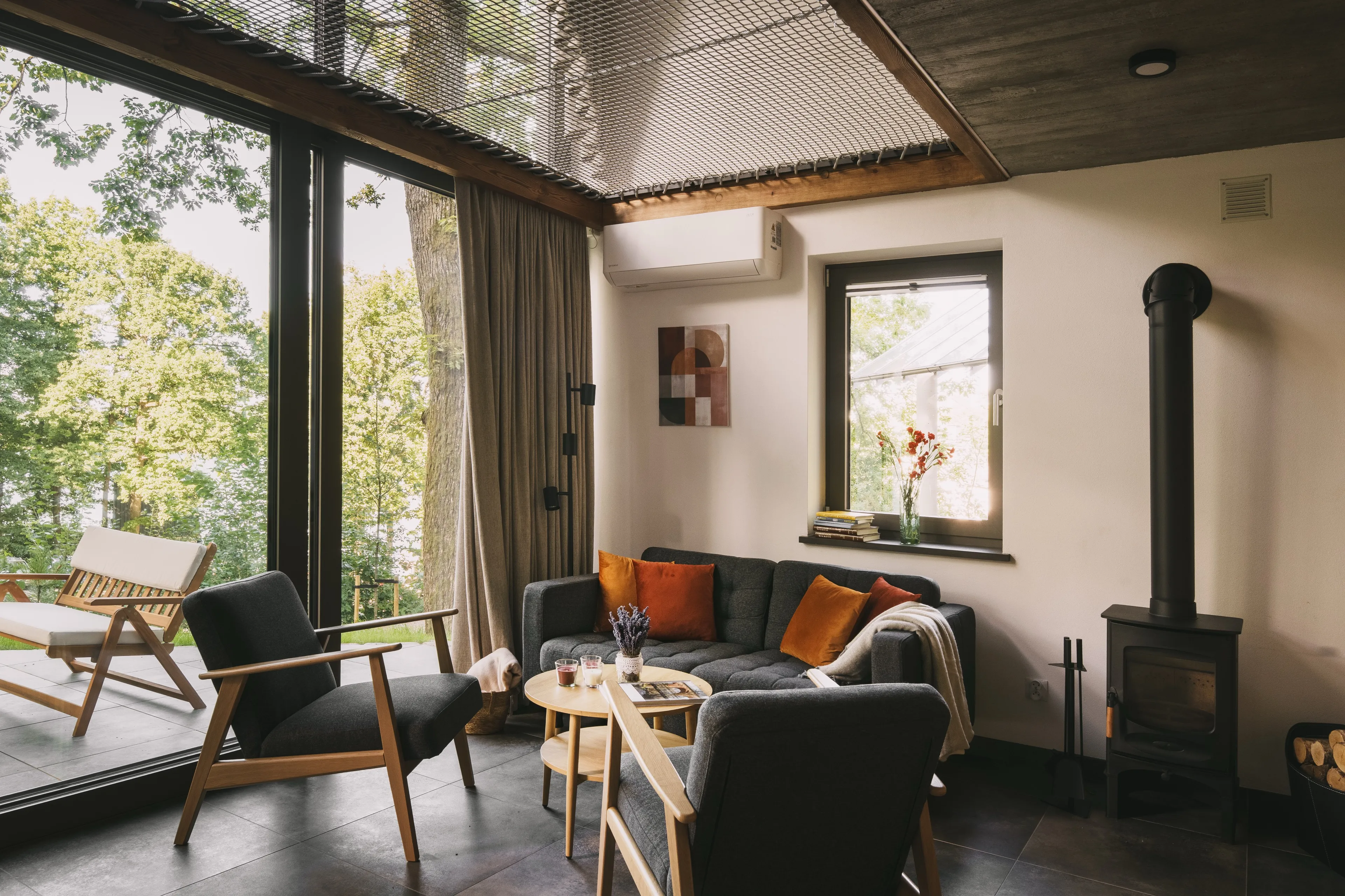 Cabin living room with a glazed wall onto the forest, wood stove and low seating